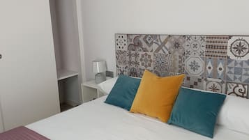Una cama con ropa de cama blanca y tres almohadas en azul, amarillo y verde azulado.
