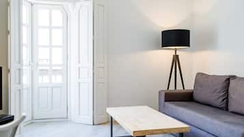 Una habitación con una puerta blanca, un sofá gris, una mesa de madera y una lámpara de pie.
