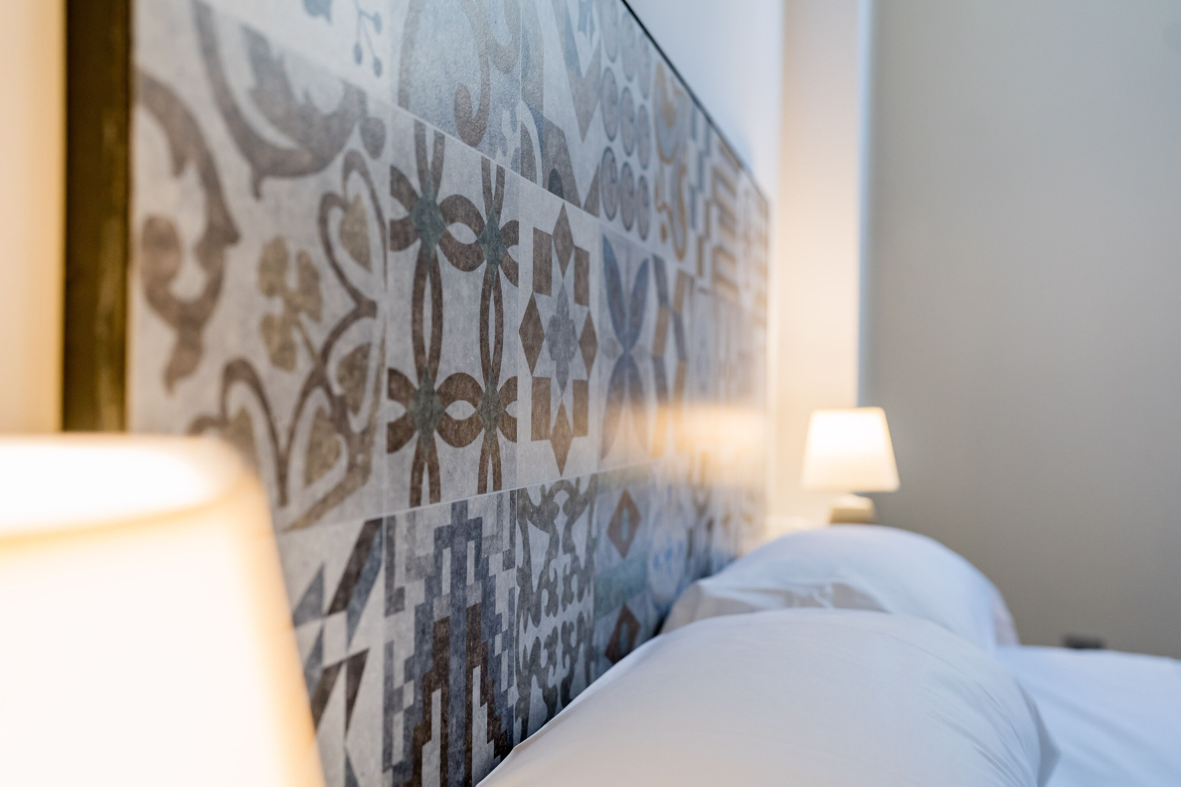 A bed with white bedding and a headboard with a patterned tile design.