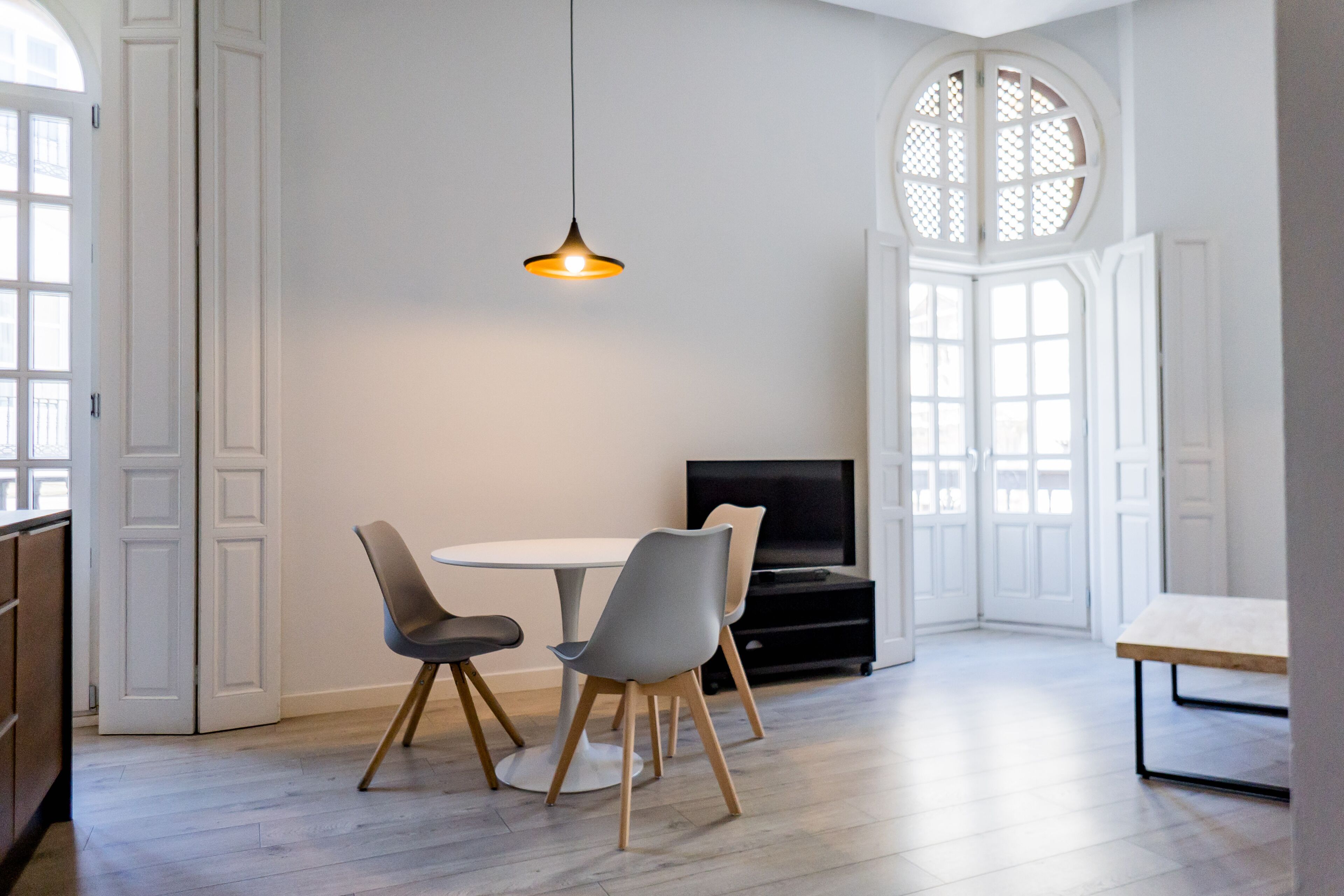 A modern dining area with a round table, two grey chairs, and a hanging pendant light.