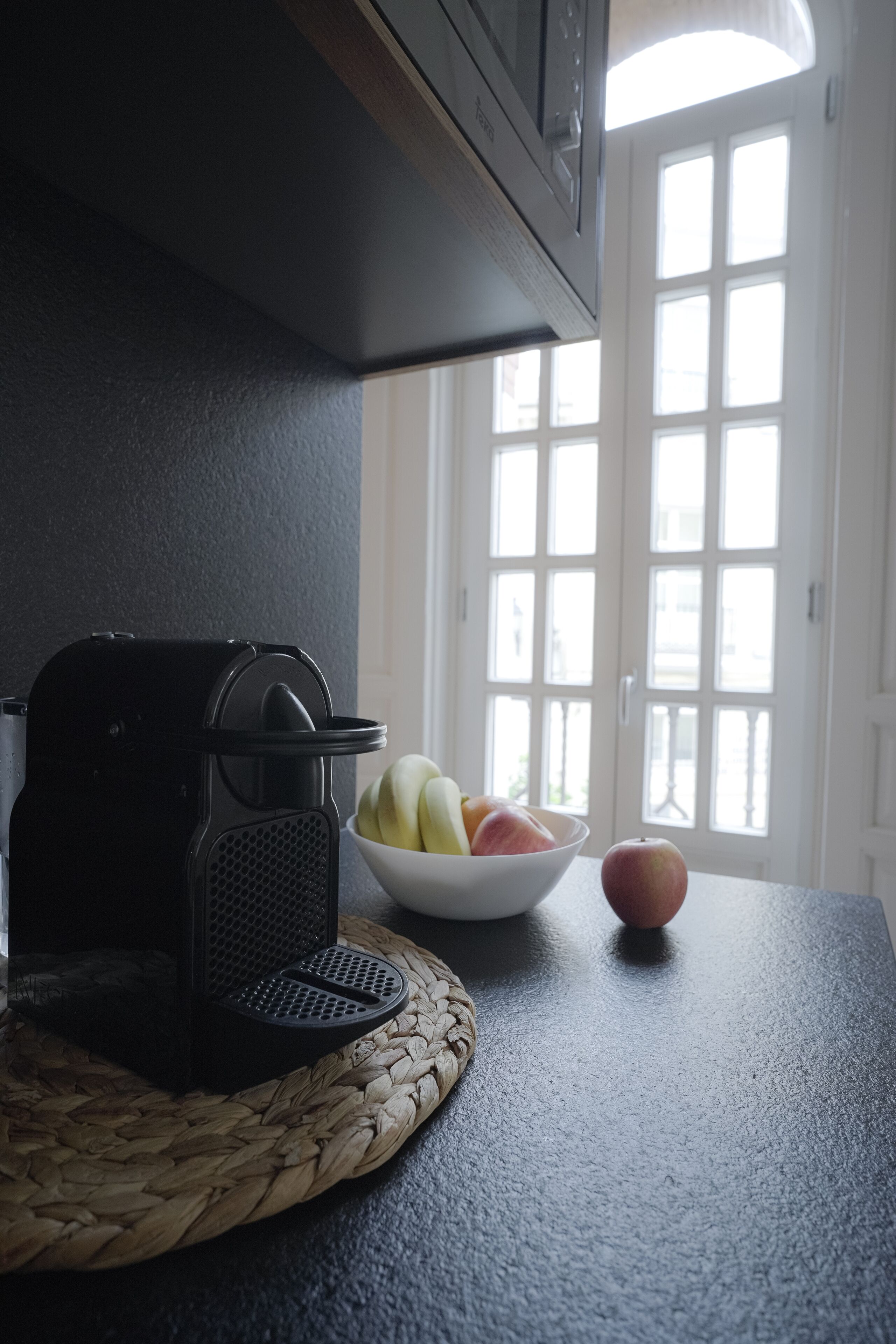 A kitchen counter with a coffee maker, a bowl of fruit, and a single apple.