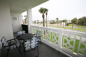 Enjoy the view from this balcony with a round table and four chairs, overlooking palm trees and a grassy area.