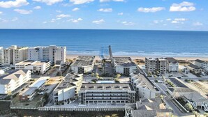Una zona urbana costera amb una combinació d'edificis residencials i comercials, una platja al fons i un cel serè.