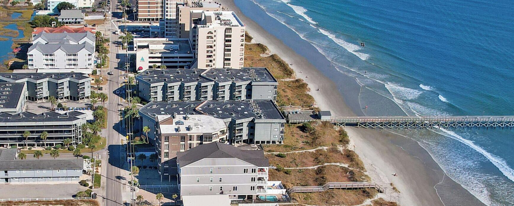 Vue aérienne d’un complexe hôtelier situé sur la côte, avec plusieurs bâtiments, une plage et un pont.