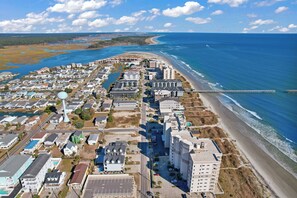 Vue aérienne d’une ville côtière avec une plage, une jetée et divers bâtiments.