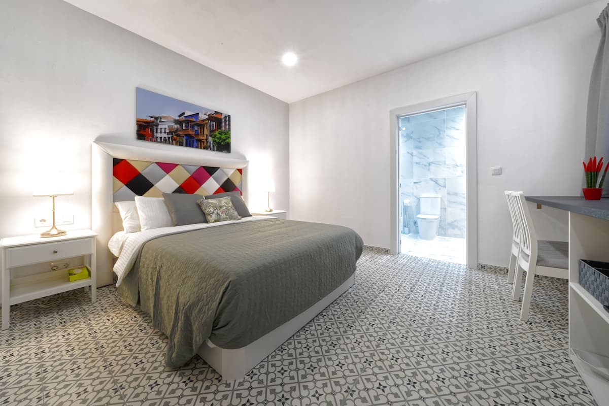 A bedroom with a bed, a nightstand, a desk, and a window.