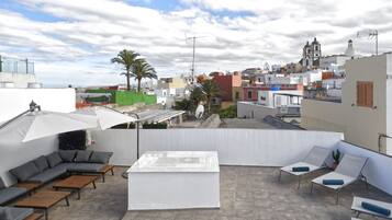 A rooftop terrace with a white sofa, lounge chairs, and a table.