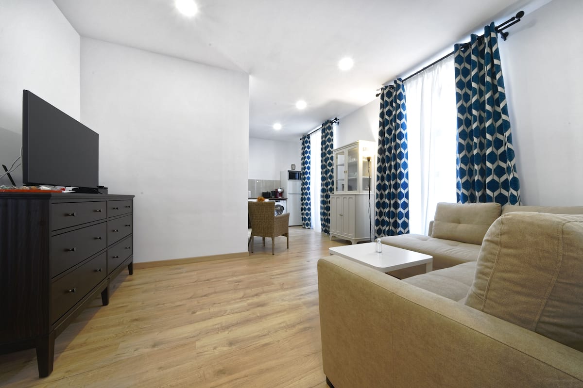 A modern living room with a sofa, a TV, and a wooden floor.