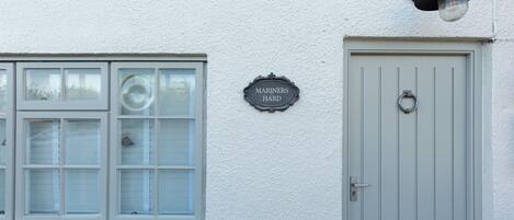 A building with a white exterior, a window with blinds, a door with a handle, and a sign reading 'MARINERS HARD'.