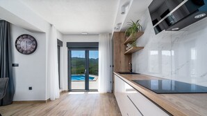 Een moderne keuken met een houten aanrecht, een inbouwfornuis en uitzicht op een zwembad door glazen deuren.