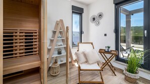Een moderne woonkamer met een houten vloer, een witte stoel met kussen, een ladder en een klein tafeltje met een plant.