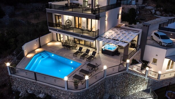 Een moderne, tweelaagse woning met een zwembad, terras en een jacuzzi.