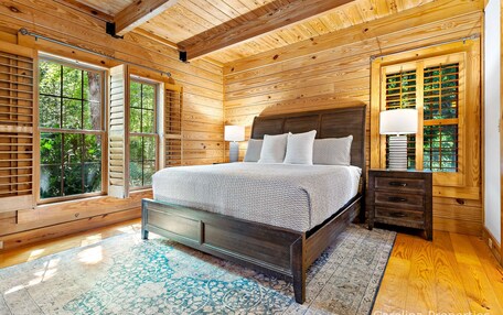 A wooden-paneled bedroom with a bed, nightstands, and large windows.
