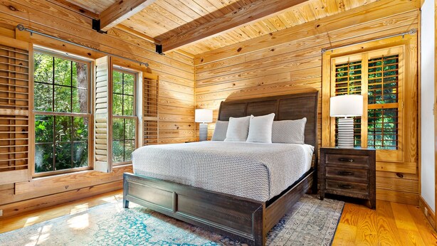 A wooden-paneled bedroom with a bed, nightstands, and large windows.
