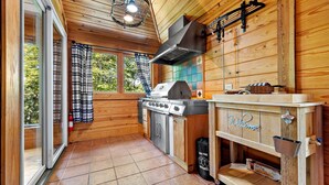 A wooden cabin kitchen with a gas stove, a built-in grill, and a 'Welcome' sign on the counter.