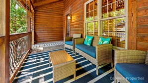 A log cabin with a porch, wicker furniture, and a view of the forest.