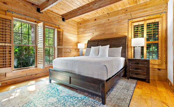 A wooden-paneled bedroom with a bed, nightstands, and large windows.