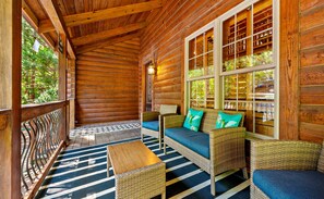 A log cabin with a porch, wicker furniture, and a view of the forest.