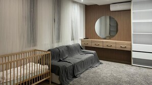 Et moderne soveværelse med en krybbe, en grå sofa, en trækommode og et stort spejl.