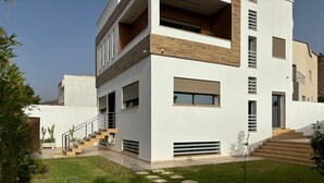 Et moderne hus i to etager med fladt tag, store vinduer og en lille forhave med haveslange og trappesten.