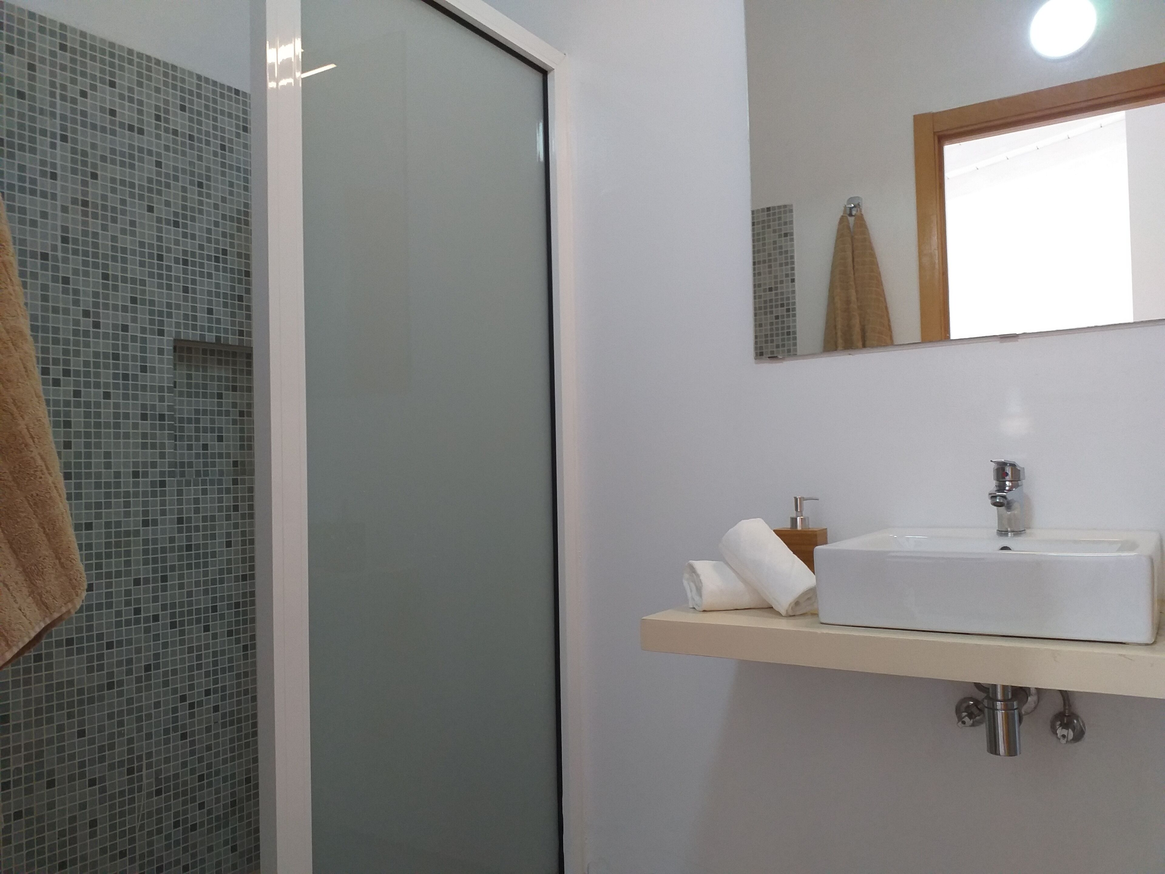 A bathroom with a glass shower door, a sink with a mirror above it, and a towel hanging on the wall.