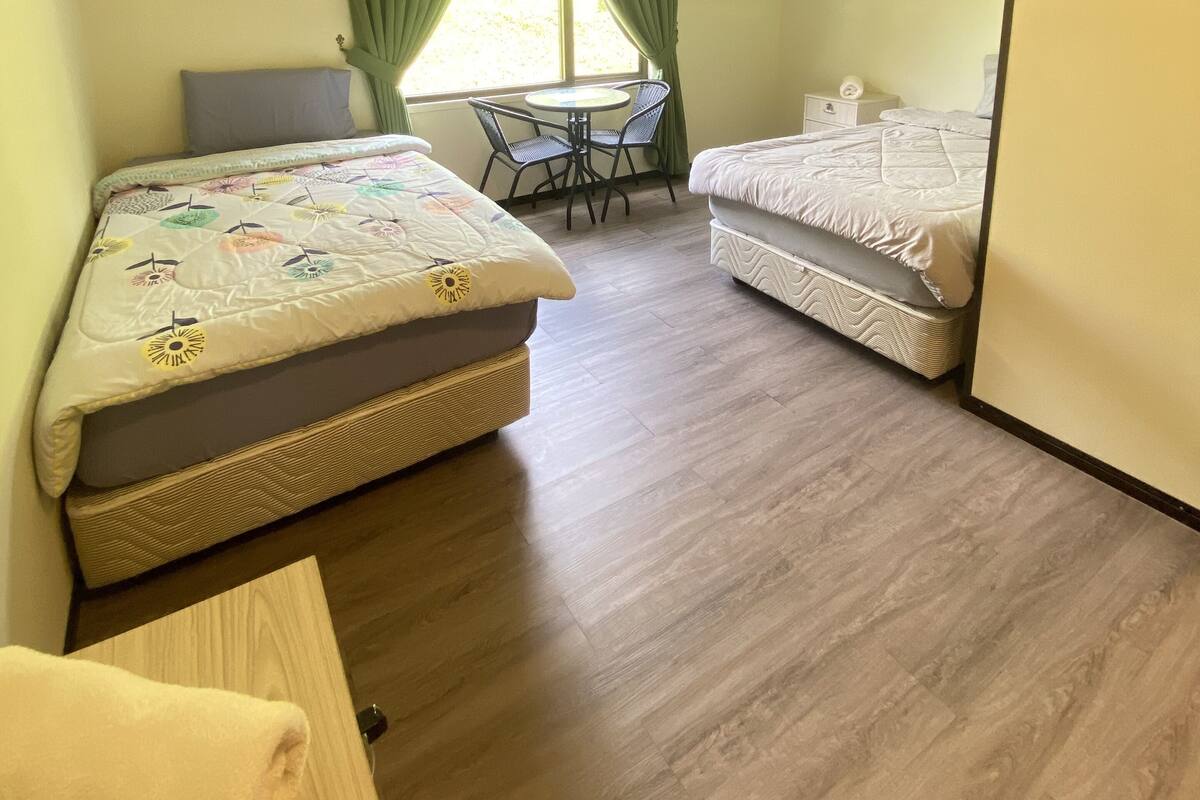 A bedroom with two beds, a small table, and a window with curtains.