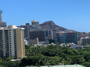 A cityscape with modern buildings, a mountain in the background, and dense greenery in the foreground.