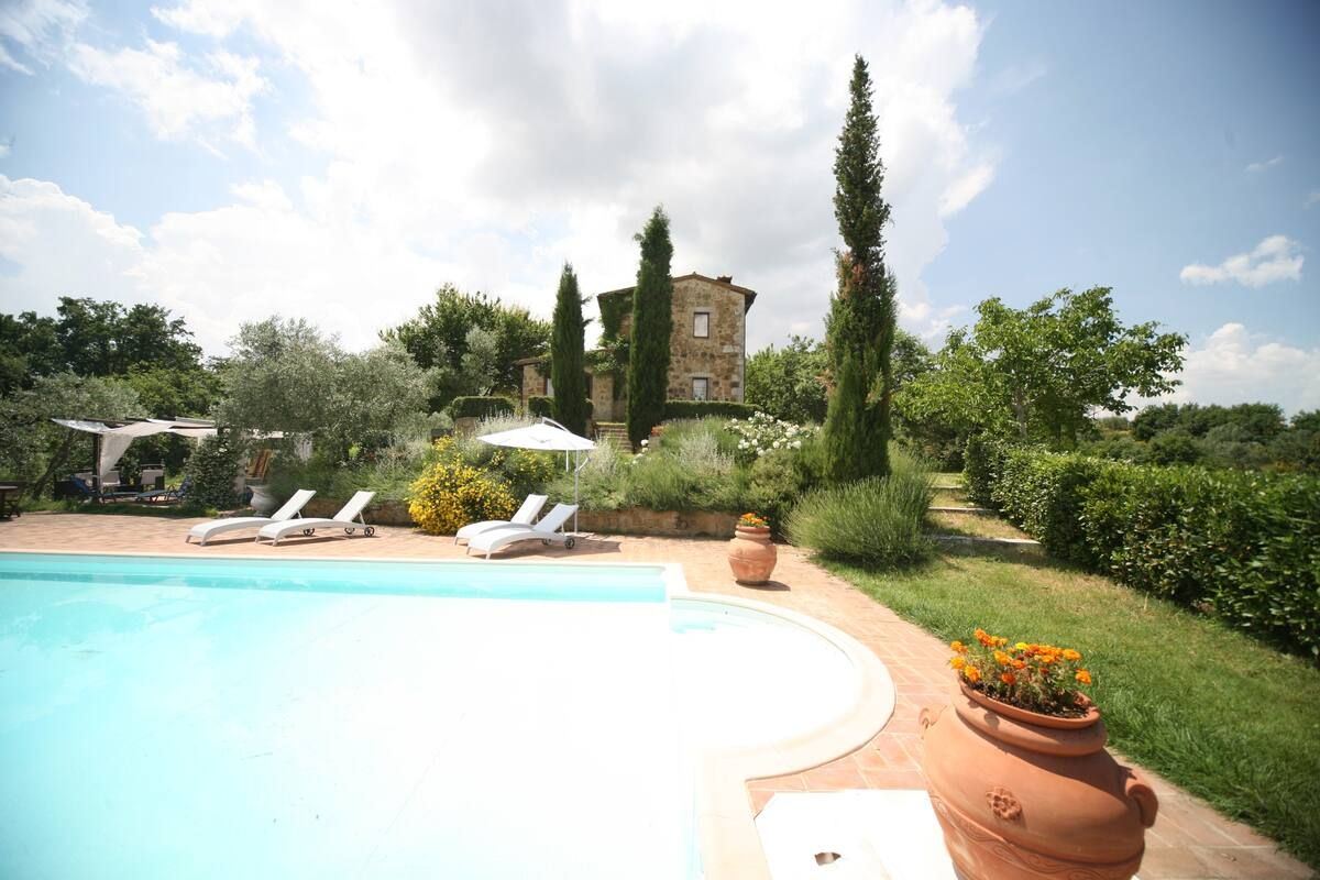A swimming pool with lounge chairs, a stone building, and a garden with various plants and a large terracotta pot.