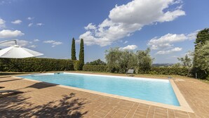 A rectangular swimming pool with a tiled deck, surrounded by greenery and a clear sky. - Eagle House (CHIANCIANO)