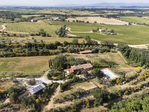 Vista aérea de una propiedad rural con viñedos, olivares y un edificio de techo rojo con piscina.