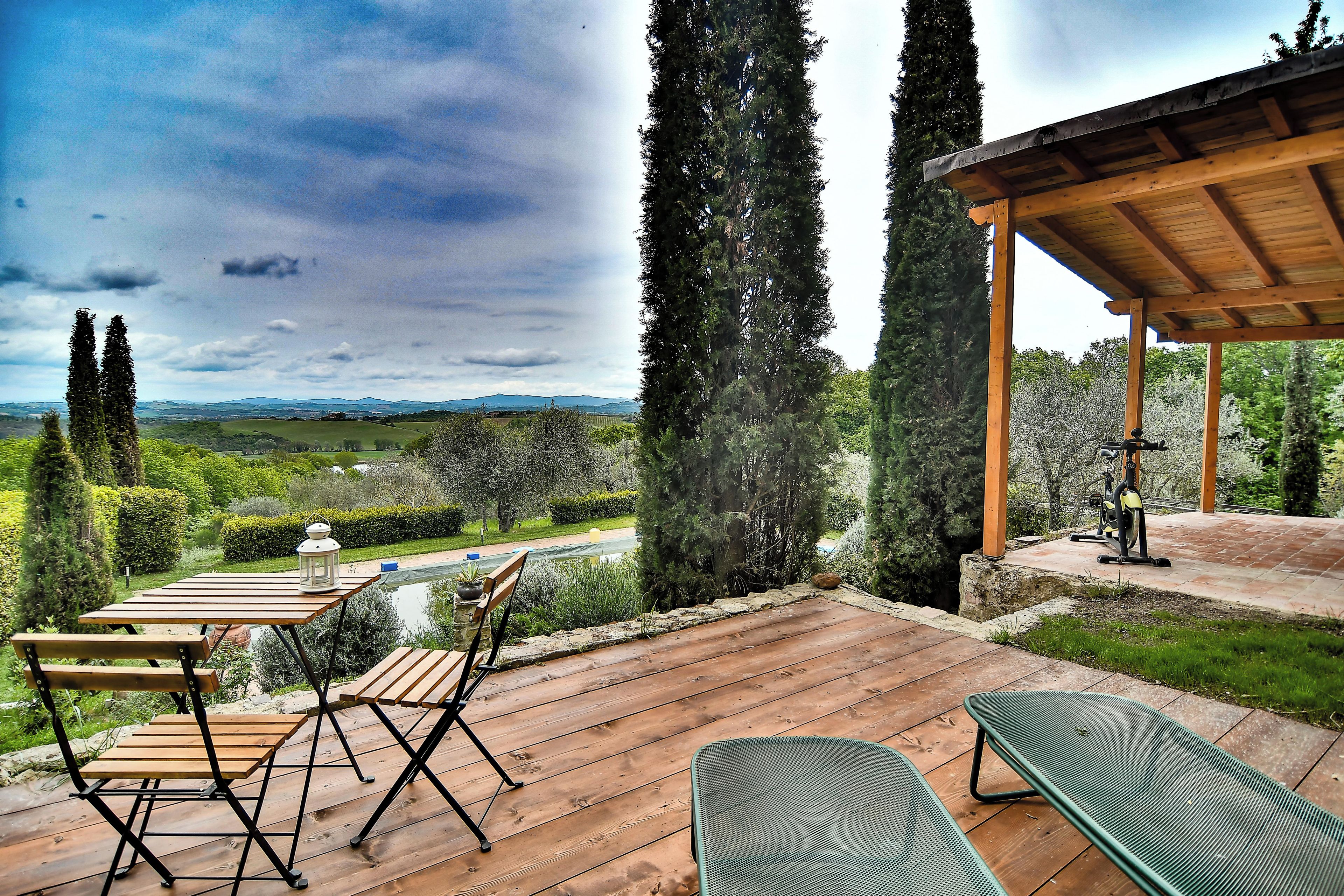 Une terrasse en bois, dotée de mobilier d’extérieur, d’une pergola et offrant une vue sur la campagne.