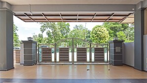 A covered entrance with a metal gate, tiled floor, and a view of trees and parked cars.