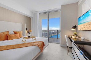 Habitación de hotel con una cama grande, un escritorio, una silla, un televisor y un balcón con vistas a la ciudad.