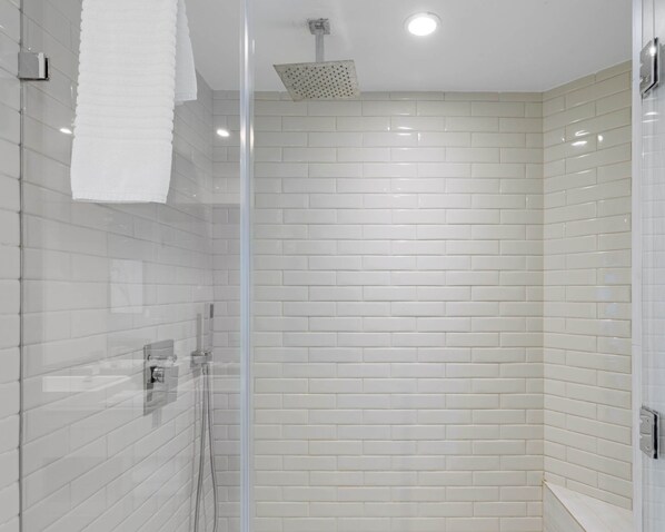 A modern bathroom with white subway tiles, a glass shower enclosure, and a visible towel rack. - Sky‑High Ocean & Bay View Luxury Condo (Hollywood)