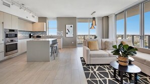 Un appartement moderne comprenant une cuisine, un coin repas et un salon. Il est doté d’une grande fenêtre, d’un canap é et d’une table basse.