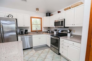A kitchen with white cabinets, stainless steel appliances, a microwave, and a dishwasher. - The Porter House - Oceanside 6 BR Home in the Heart of Duck - Private Pool, Dog Friendly (Duck)