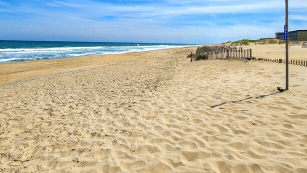 Ein sandiger Strand mit einer Holzlattenzaun und einem Schild mit der Aufschrift 'SMALL'.