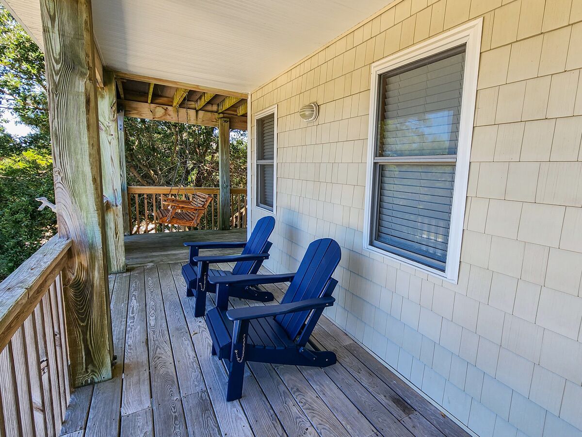 Eine überdachte Veranda mit zwei Adirondack-Stühlen und einer Holzterrasse.