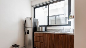 Een kleine keuken met een roestvrijstalen koelkast, houten kastjes, een granieten aanrechtblad en een raam dat natuurlijk licht binnenlaat.