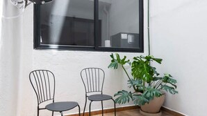 Een kleine, lichte kamer met twee metalen stoelen, een groot raam en een potplant.