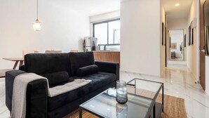 Een moderne woonkamer met een zwarte bank, een glazen salontafel en een hanglamp.