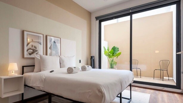 A modern hotel room with a large bed, a nightstand with a lamp, a sliding glass door to a balcony, and two framed artworks on the wall. - w* | Upscale 1BR with Amazing Deco in Polanco (Ciudad de México)