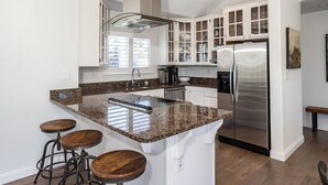 A kitchen with white cabinets, a stainless steel refrigerator, granite countertops, and wooden stools. - Luxury Living at the Beach (Stinson Beach)