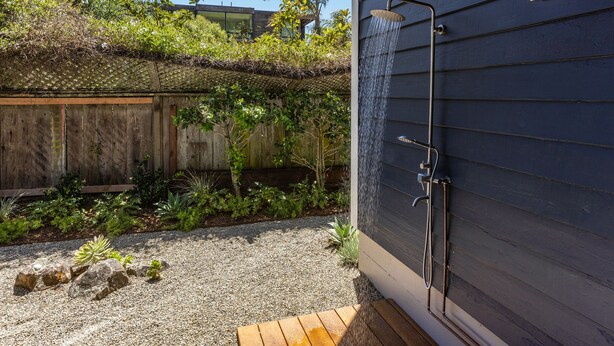 A modern outdoor shower area with a wooden deck, a gravel path, and lush greenery. - Luxury Living at the Beach (Stinson Beach)