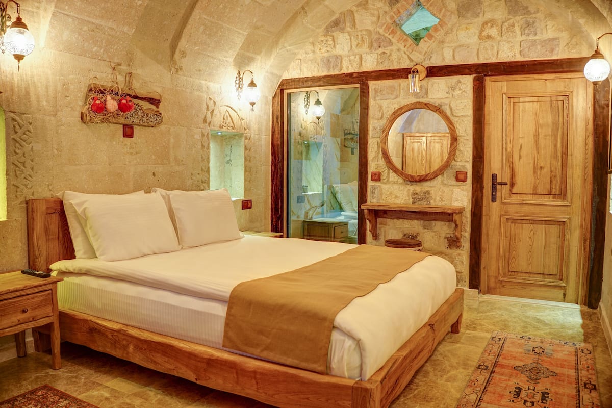 A bedroom with a wooden bed, a nightstand, a mirror, and a stone wall.