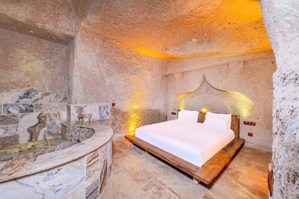 A stone-walled bedroom with a bed, a stone bathtub, and a marble sink.