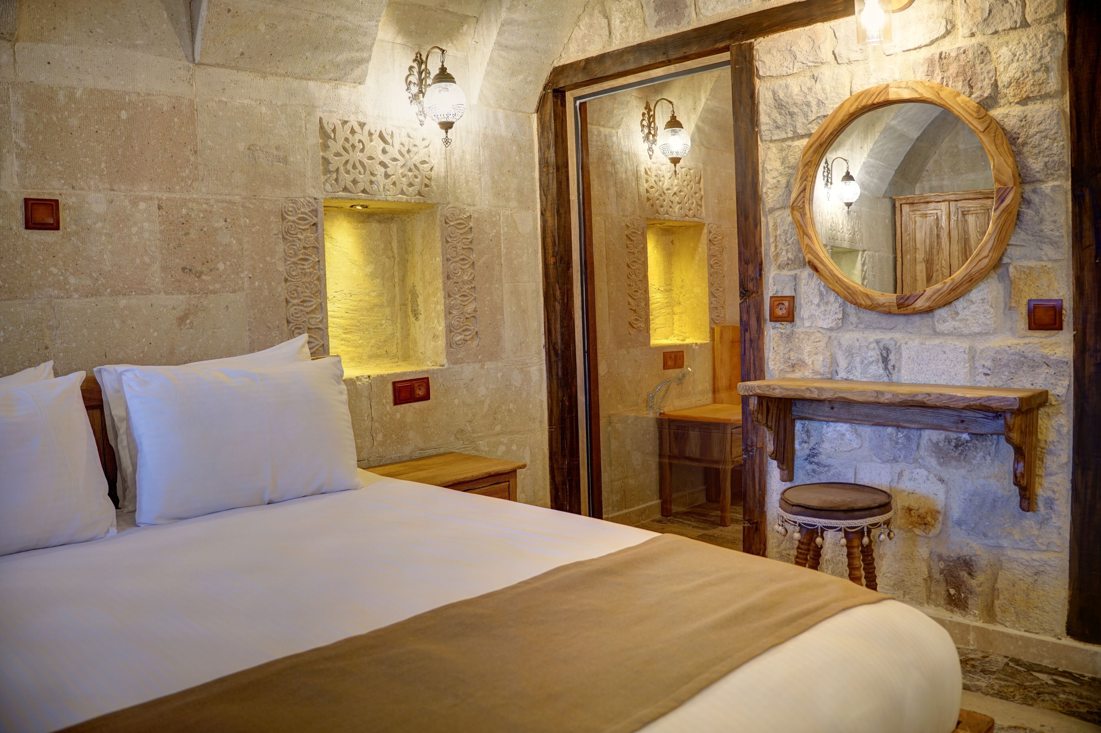 Un dormitorio con una cama grande, paredes de piedra, un aparador de madera y un espejo.