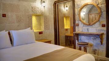 Un dormitorio con una cama grande, paredes de piedra, un aparador de madera y un espejo.