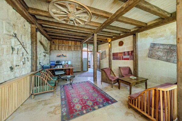 A rustic interior with exposed wooden beams, a stone wall, a wooden crib, a patterned rug, and a small table. - The Calypso Cave (Ürgüp)
