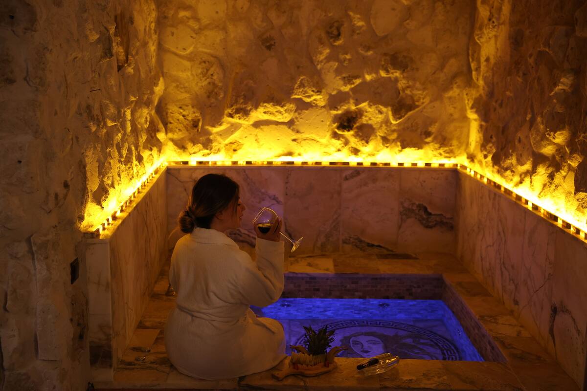 A person sitting in a stone-walled room with a heated floor, holding a glass.